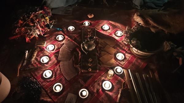 Círculo de velas encendidas y cartas alrededor de un altar, en penumbra